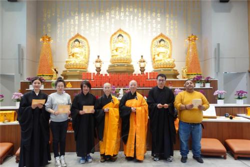 新發心信眾拿著皈依證喜與法師合照，（由左至右）李璿、高漫、于雅靜、永超法師、妙祥法師、張翰一及塞爾維亞籍Zivojin Radivojevic